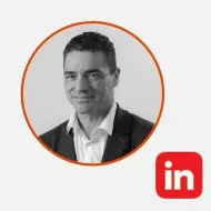 Retrato en blanco y negro de un hombre sonriente con blazer, dentro de un círculo naranja. El logotipo de LinkedIn aparece en la esquina inferior derecha.